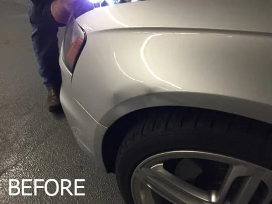A large dent in the front fender of a silver car before repair