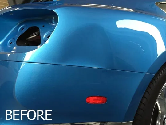 A deep dent in the rear quarter panel of a blue car before repair